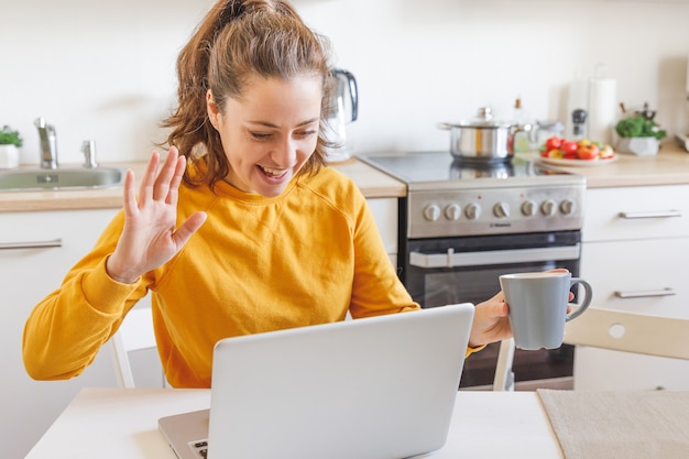 Smiling girl waving hand video calling family by webcam