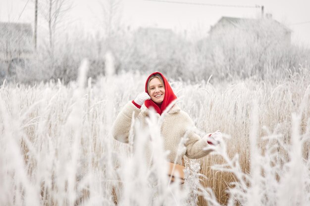 Foto una ragazza sorridente con una pelliccia bianca posa tra cespugli innevati