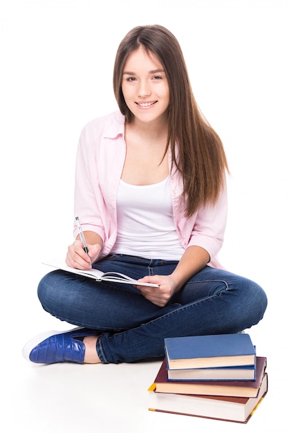 Smiling girl with books is sitting on the floor.