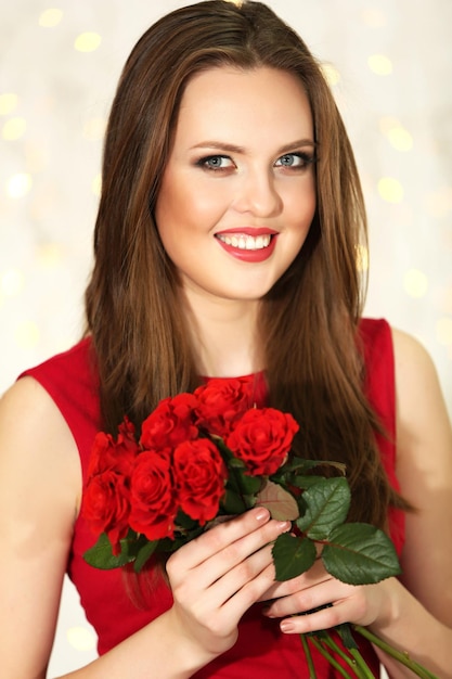 Foto ragazza sorridente con bouquet di rose rosse su sfondo di luci