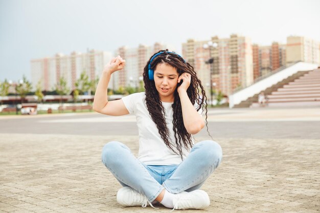 A smiling girl with dreadlocks in headphones is sitting on the
floor in the park a happy young woman relaxing with headphones
enjoying music space for copyinggeneration z