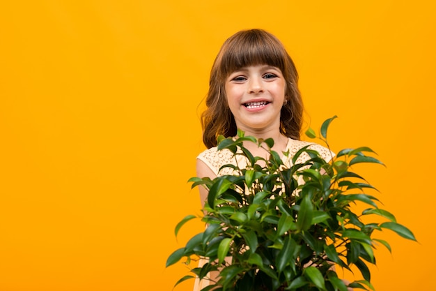 smiling girl with flower in pot on orange isolated wall close-up