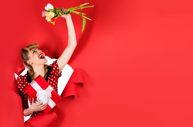 Smiling girl with flowers and gift. Woman with tulips and Present looking through hole. Copy space for advertising.