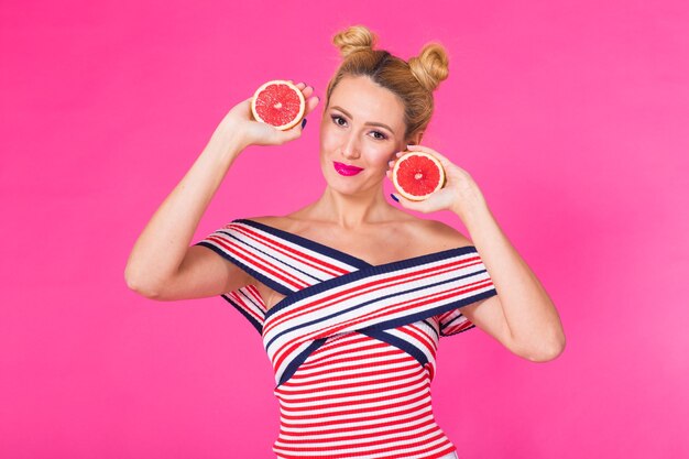 Smiling girl with grapefruit cut in half fruit in hand on pink background