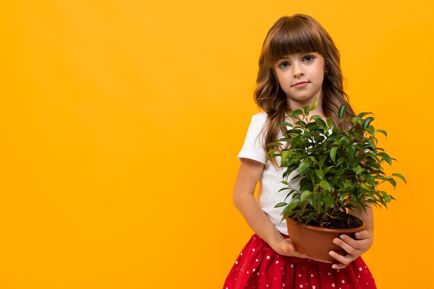 Smiling girl with green plant on orange isolated background close-up.