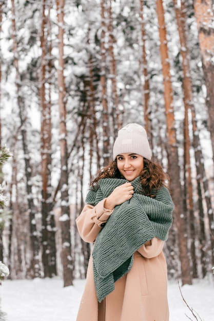 코트에 녹색 스카프를 두른 웃는 소녀가 겨울에 눈 속에 서 있다