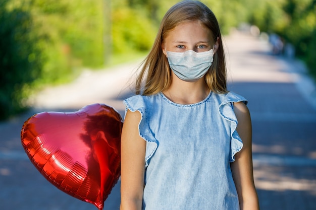 Smiling girl with heart balloon in a medical mask on the face