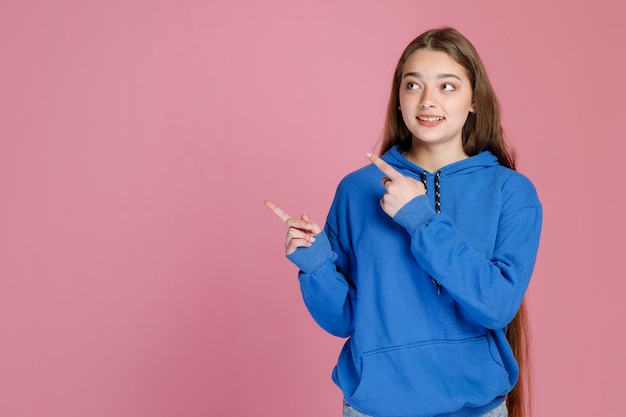 Foto ragazza sorridente con lunghi capelli biondi che puntano lontano con le dita che mostrano la direzione mentre guardano in alto