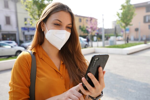 Smiling girl with mask checking her phone on street