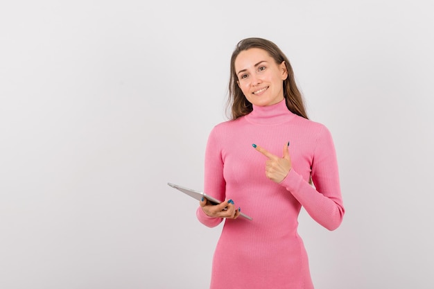 Smiling girl with tablet computer is pointing to left with forefinger on white background