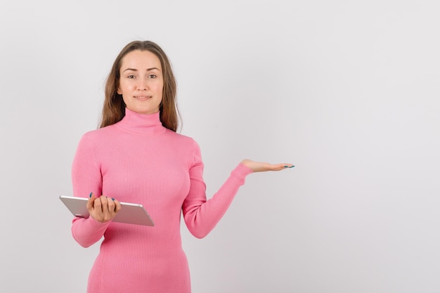 Smiling girl with tablet computer is pointing to right with hand on white background