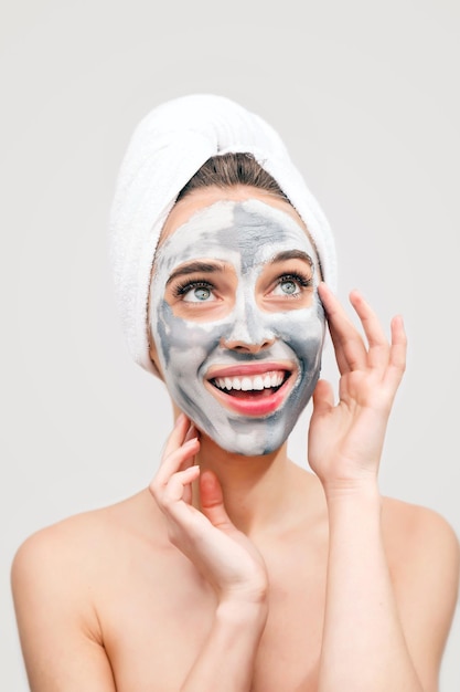 Photo smiling girl with towel ob the head applies white nourishing cream on face