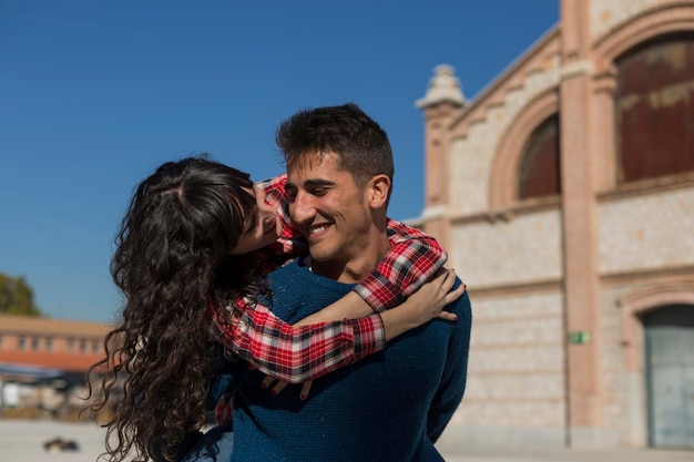 Smiling girlfriend embracing boyfriend in city