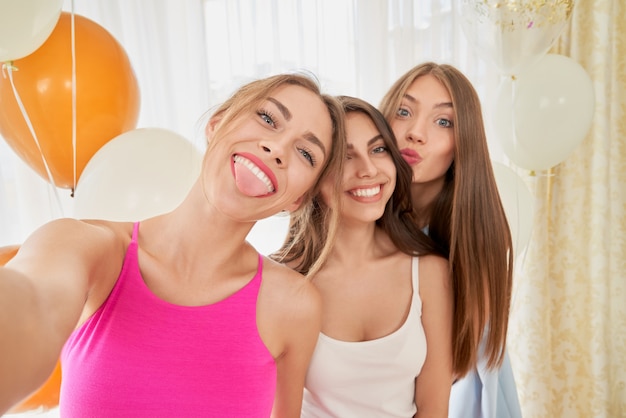 Smiling girlfriends taking selfie, making faces.