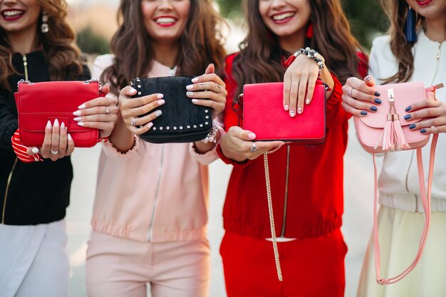 Улыбающиеся подружки с маникюром держат сумочки.
