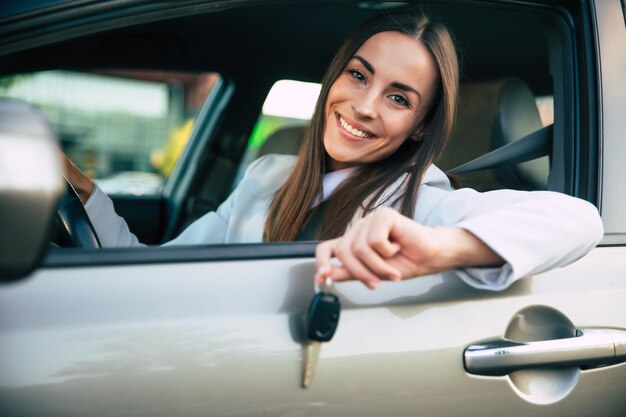 この購入をテストしている間、笑顔のゴージャスな若いビジネスウーマンは彼女の新しい車から手に鍵を持っています