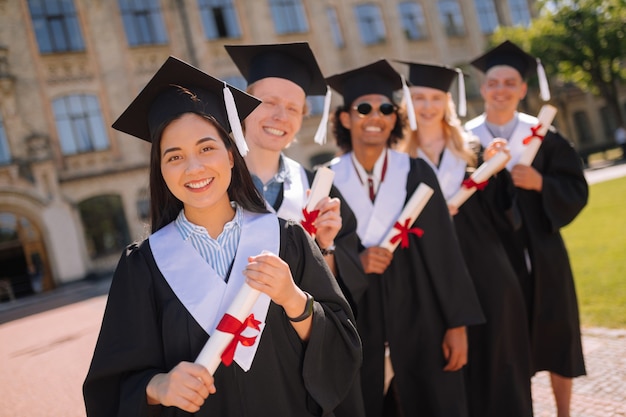 Smiling graduates holding their diplomas with red ribbons on them