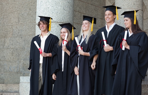 Smiling graduates posing while holding their diploma