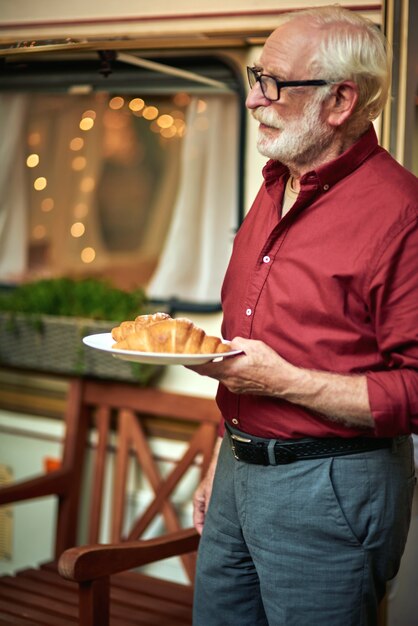 Smiling gray haired man with glasses going to have breakfast with a croissant