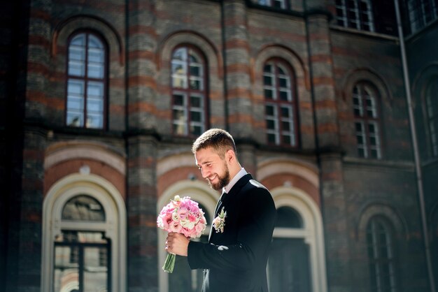 笑顔の新郎は、彼の腕の中にピンクの結婚式の花束を見て