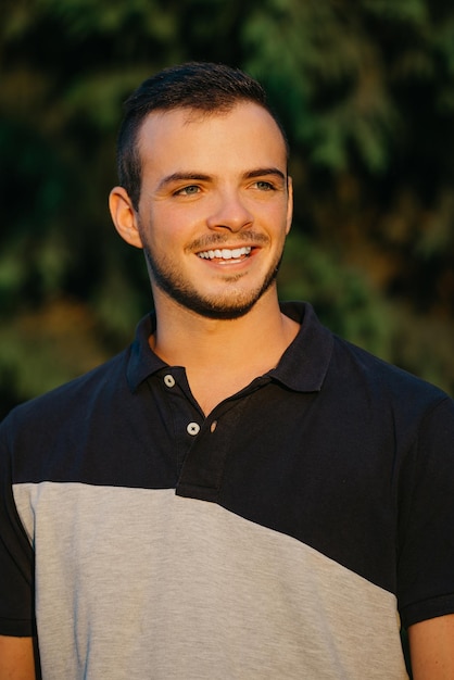 A smiling guy is posing with green bushes in the background