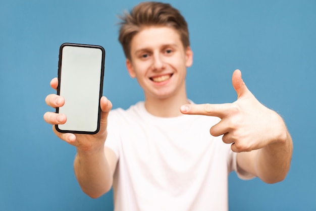 Фото Улыбающийся парень указывает пальцем на смартфон с белым экраном.