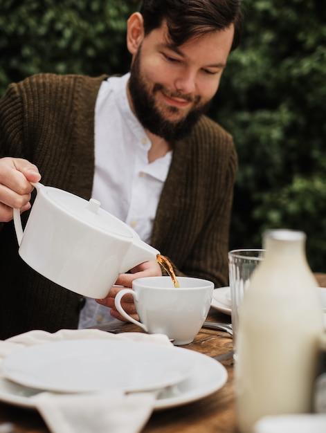 微笑む男はお茶を注ぎます。自然の中で朝食、英国式