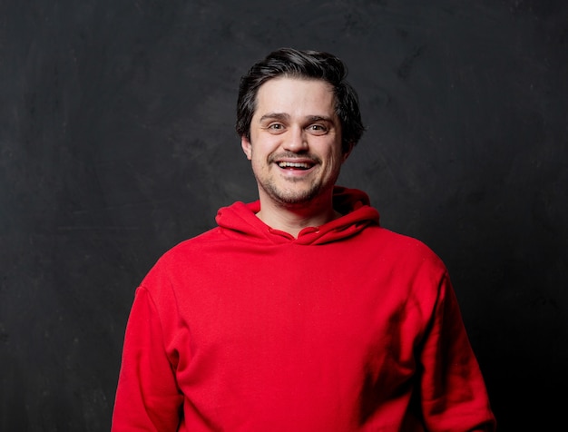 Smiling guy in red sweatshirt on dark wall