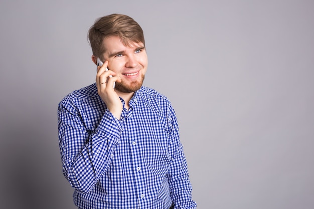 Smiling guy talking on a mobile phone on gray wall