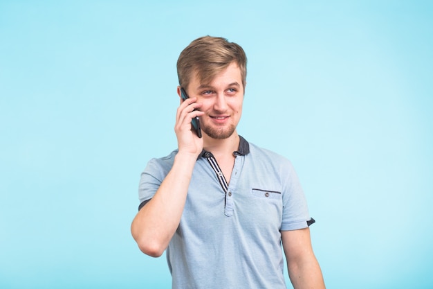 Улыбающийся парень разговаривает по мобильному телефону, изолированному на синем