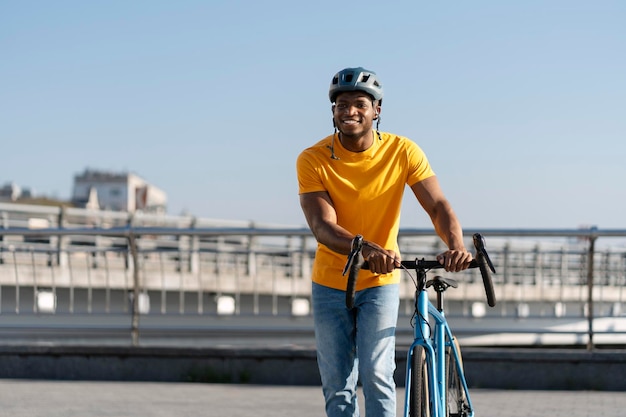 smiling handsome African rider wearing protective helmet rides bicycle on urban street outdoors