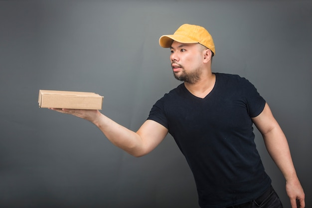 Smiling handsome asian delivery man wearing cap, giving and carrying parcel, cardboard box, Moving house day and express delivery concept 