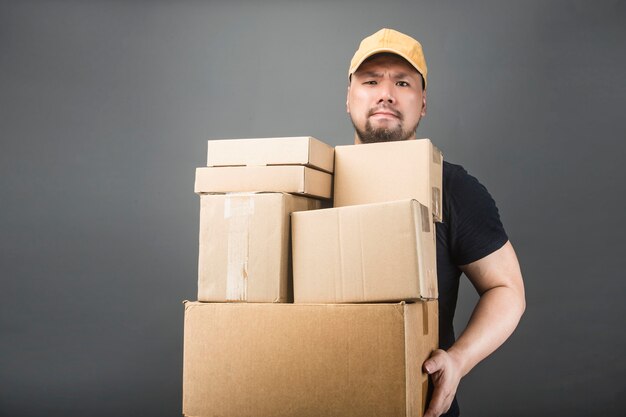 Smiling handsome asian delivery man wearing cap, giving and carrying parcel, cardboard box, Moving house day and express delivery concept 