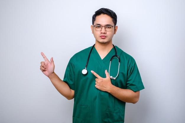 Smiling handsome asian doctor nurse in scrubs and stethoscope pointing fingers upper left corner showing online clinic banner