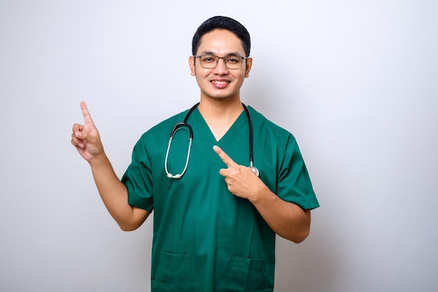 Sorridente infermiere medico asiatico bello in scrub e stetoscopio che punta le dita nell'angolo in alto a sinistra che mostra il banner della clinica online