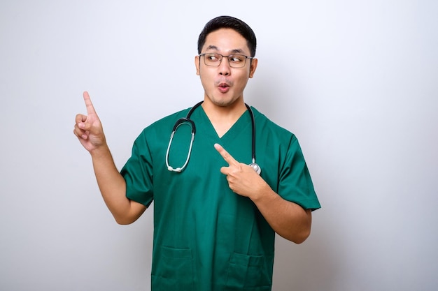 스크럽과 청진기에서 웃는 잘 생긴 아시아 의사 간호사가 온라인 클리닉 배너를 보여주는 왼쪽 상단 모서리를 가리키는 청진기
