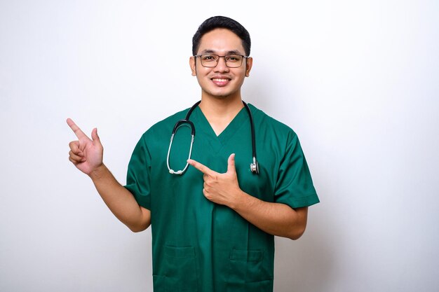 Smiling handsome asian doctor nurse in scrubs and stethoscope pointing fingers upper left corner showing online clinic banner