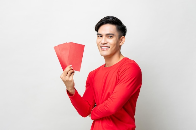 Smiling handsome Asian man holding red envelopes or Ang Pow in studio isolated gray background for Chinese new year concepts