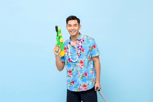 Улыбающийся красивый азиатский мужчина играет с водяной пушкой для фестиваля Сонгкран в Таиланде и Юго-Восточной Азии