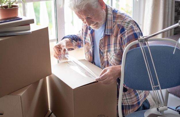 Photo smiling handsome bearded senior man closing cardboard box in moving day concept of relocating