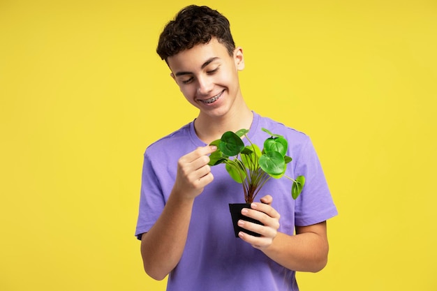 Smiling handsome boy wearing colorful clothes holding flower pot isolated on yellow background