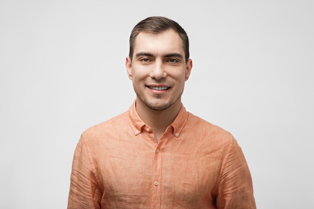 Smiling handsome man about 30 years old in orange shirt on white background male portrait