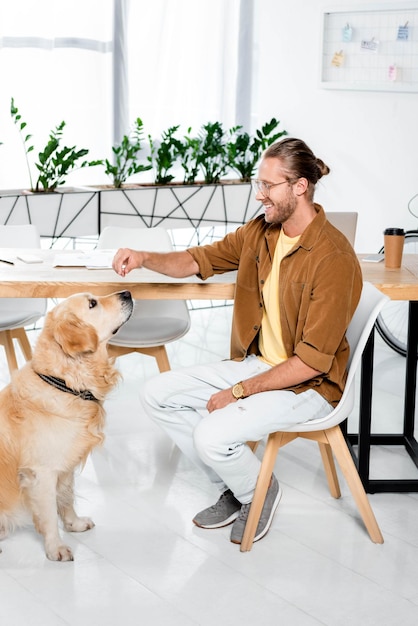 Smiling and handsome man feeding cute golden retriever in office