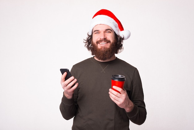 웃는 잘 생긴 남자는 흰색 배경 위에 컵과 그의 전화를 갈 잡고있다.