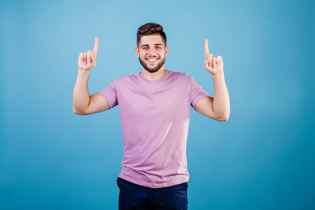 Smiling handsome man pointing finger at copy space isolated on blue