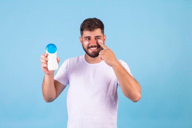 Smiling handsome man putting on sunscreen on blue background with free space for text Summer and holiday care