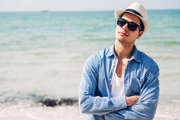 笑顔のハンサムな男は、熱帯のビーチでサングラスと麦わら帽子でリラックスします。夏の休暇