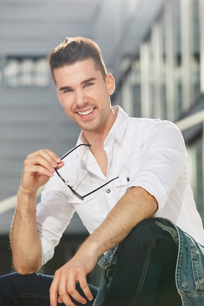 Smiling handsome man sitting in city with sunglasses