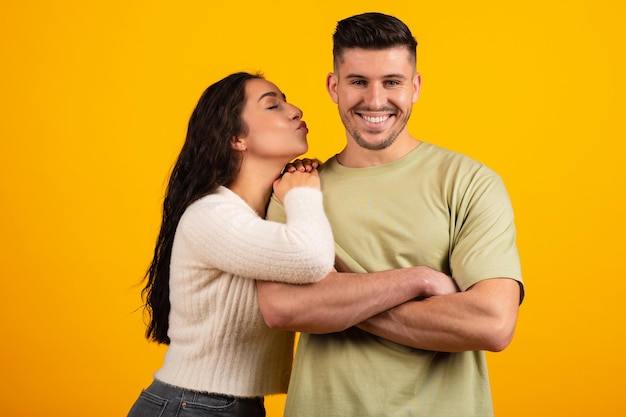 Smiling handsome millennial middle eastern woman kissing tall boyfriend on cheek have fun together
