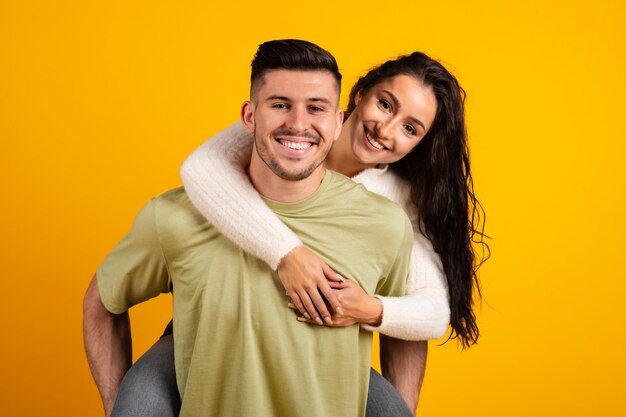 Smiling handsome millennial strong arab guy hold lady on back have fun together